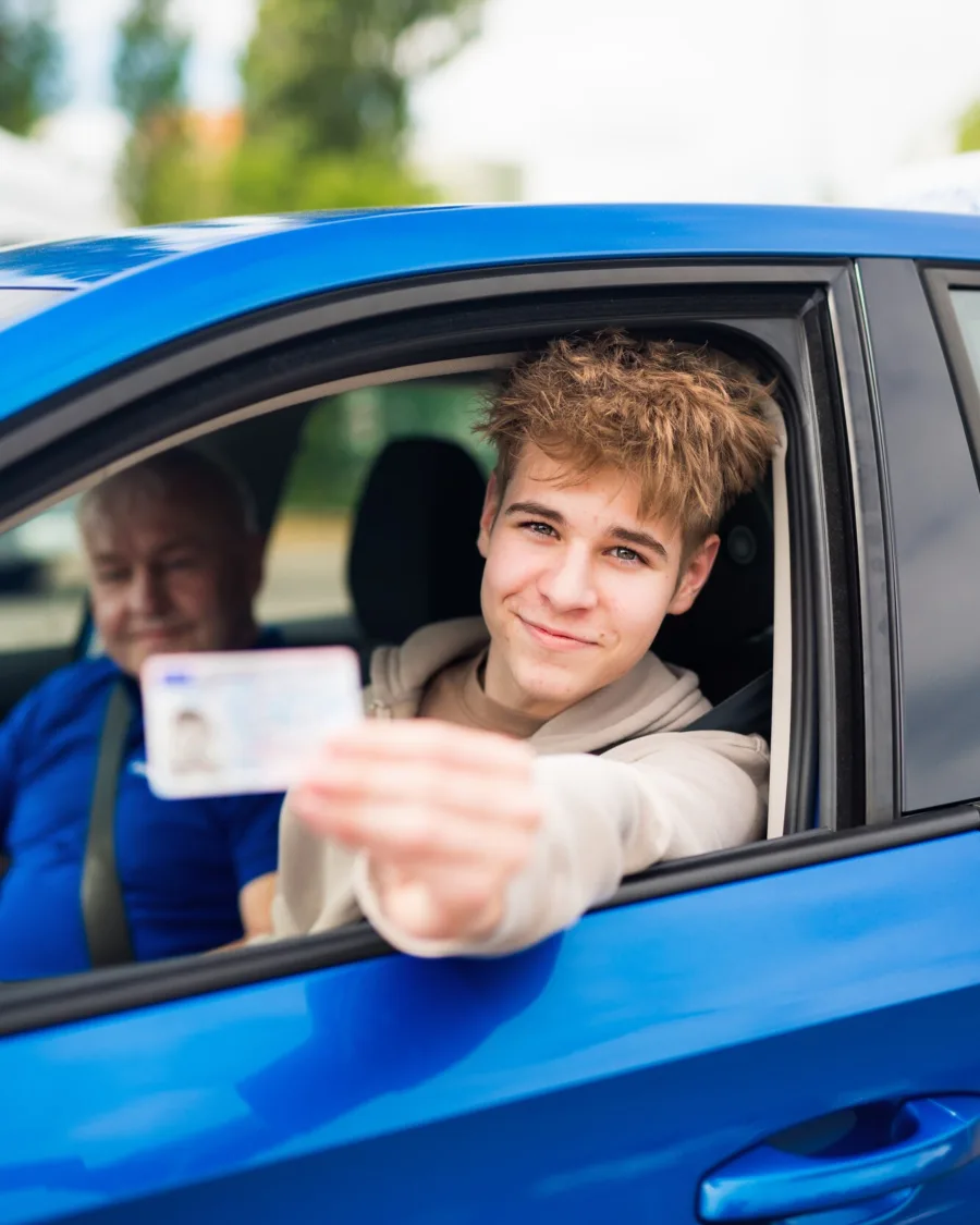 Mladý absolvent ukazuje řidičák z okna modré Škody Fabia CJ Autoškoly